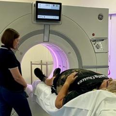 a person lies on a bed with their feet in a round machine and another person stands nearby
