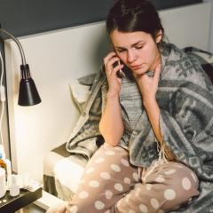 Lady on phone while sitting in bed with hand on throat